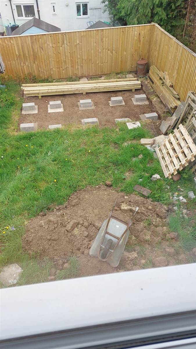 Concrete pad footings laid out in a grid across the garden, treated timber stacked alongside ready to use